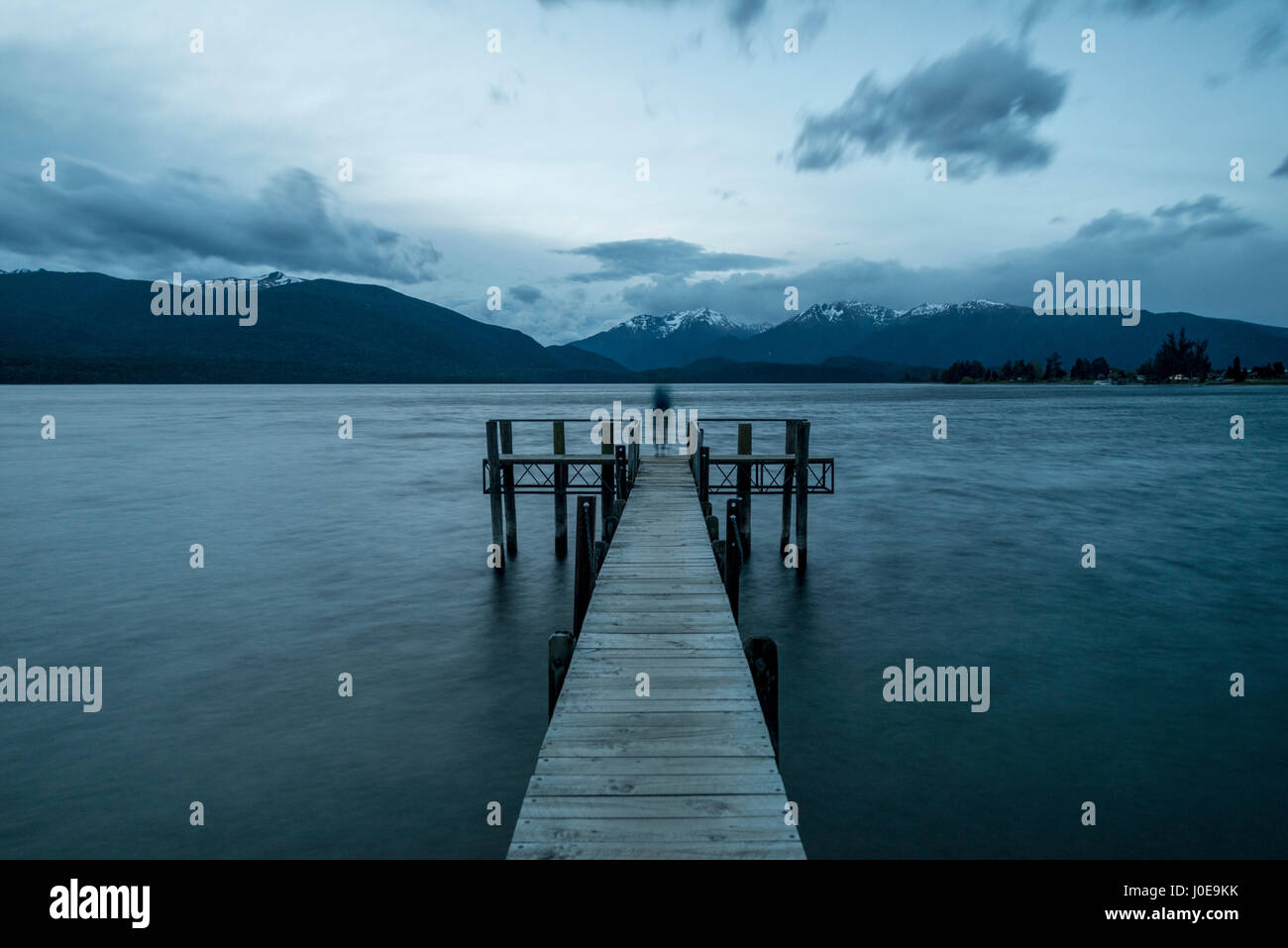 Cloudy sky over mountains, silhouette standing on dock, Lake Te Anau, Southland, New Zealand Stock Photo