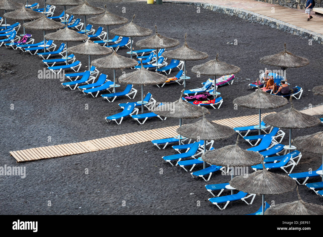 CALLAO SALVAJE, TENERIFE, CANARY, SPAIN-CIRCA JAN, 2016: Blue sunbeds and straw parasols are on the Playa de Ajabo beach. Atlantic ocean. Small public Stock Photo