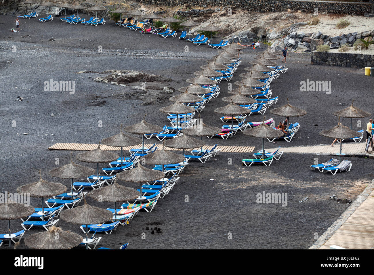 CALLAO SALVAJE, TENERIFE, CANARY, SPAIN-CIRCA JAN, 2016: Blue sunbeds and strawy parasols are on the Playa de Ajabo beach. Atlantic ocean. Public beac Stock Photo