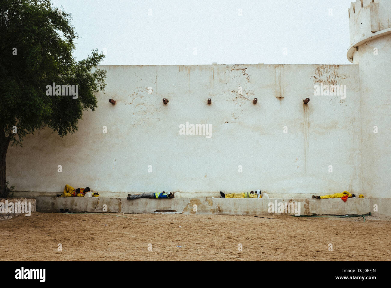 Blue collar workers are resting and having a nap at a wall in Doha, Qatar. Stock Photo