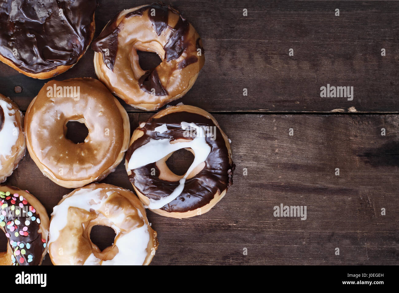 Background of chocolate, carmel, glazed and filled donuts over a rustic background with copy space. Image shot from overhead. Stock Photo