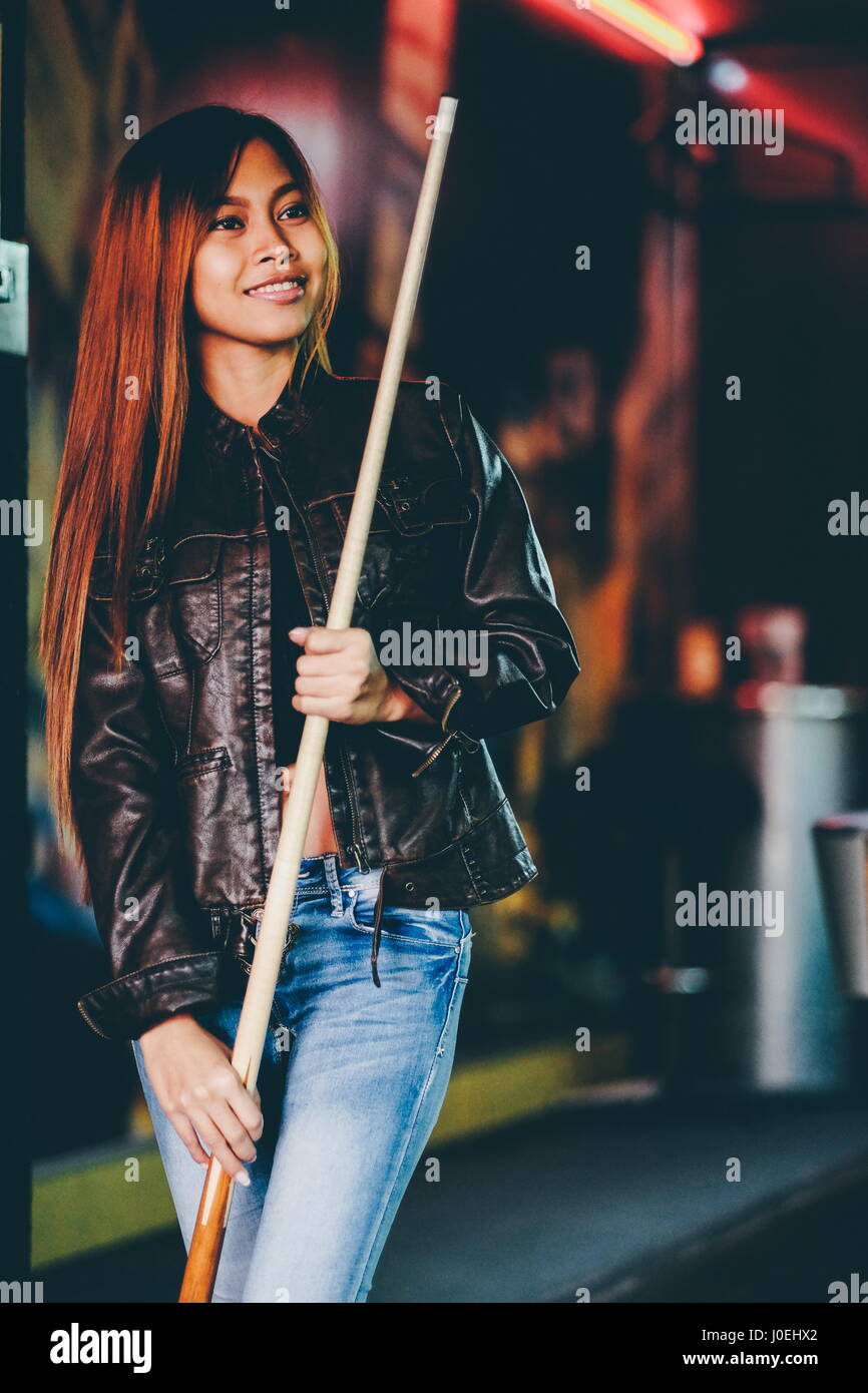 Young beautiful girl wearing leather jacket in a billiard club, with cue stick preparing for the game Stock Photo