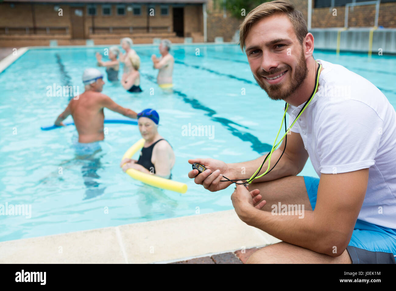 Portrait of smiling swim coach holding stopwatch near poolside Stock