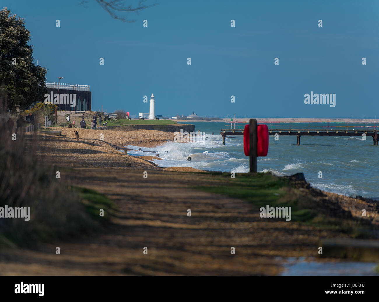 A Blustery day by the sea, people out for walks with their dogs, taking in the views of the lighthouse and beautiful scenery around them. Stock Photo
