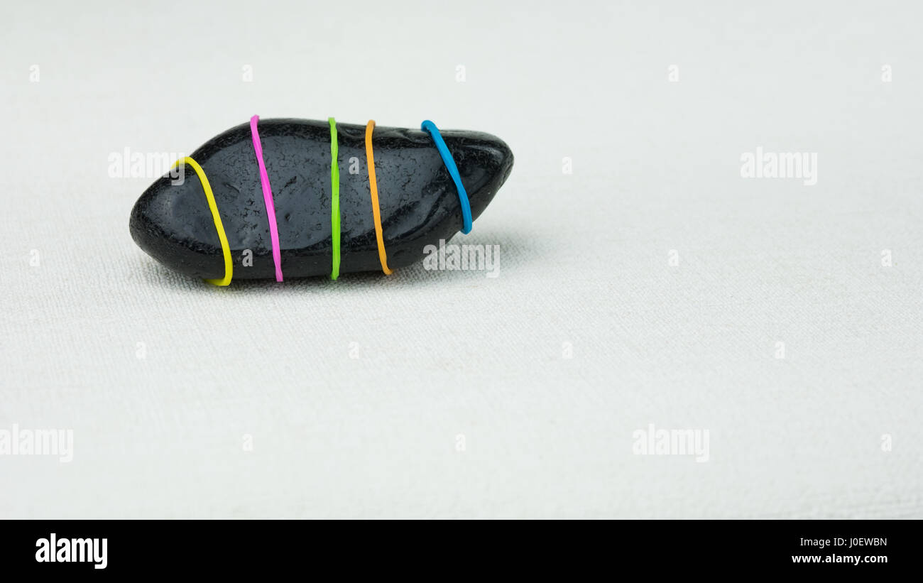 Being different one black stone with coloured stripes on bright background. Stock Photo