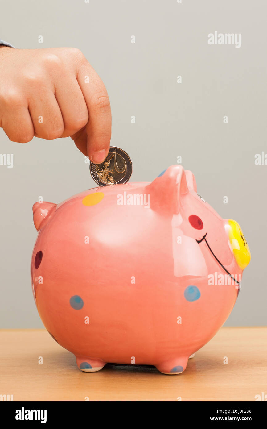 Kid's hand put a coin in a pink pig bank Stock Photo - Alamy