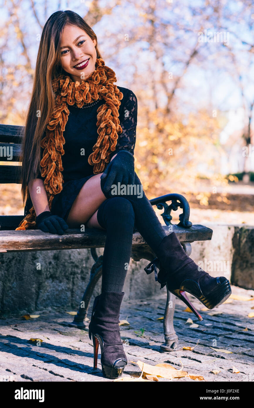 Young beautiful girl in black dress with brown scarf sitting on the bench Stock Photo