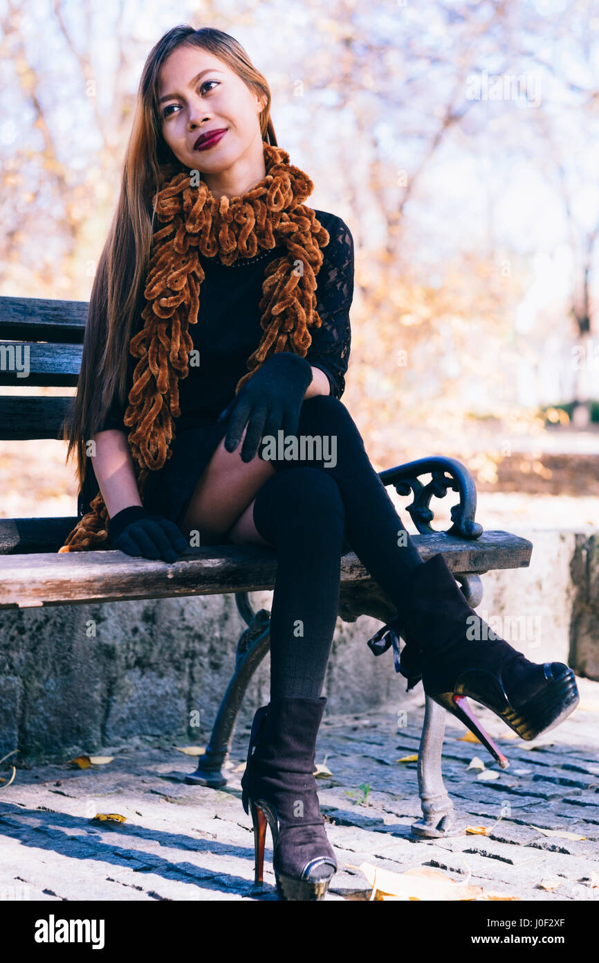 Young beautiful girl in black dress with brown scarf sitting on the bench Stock Photo