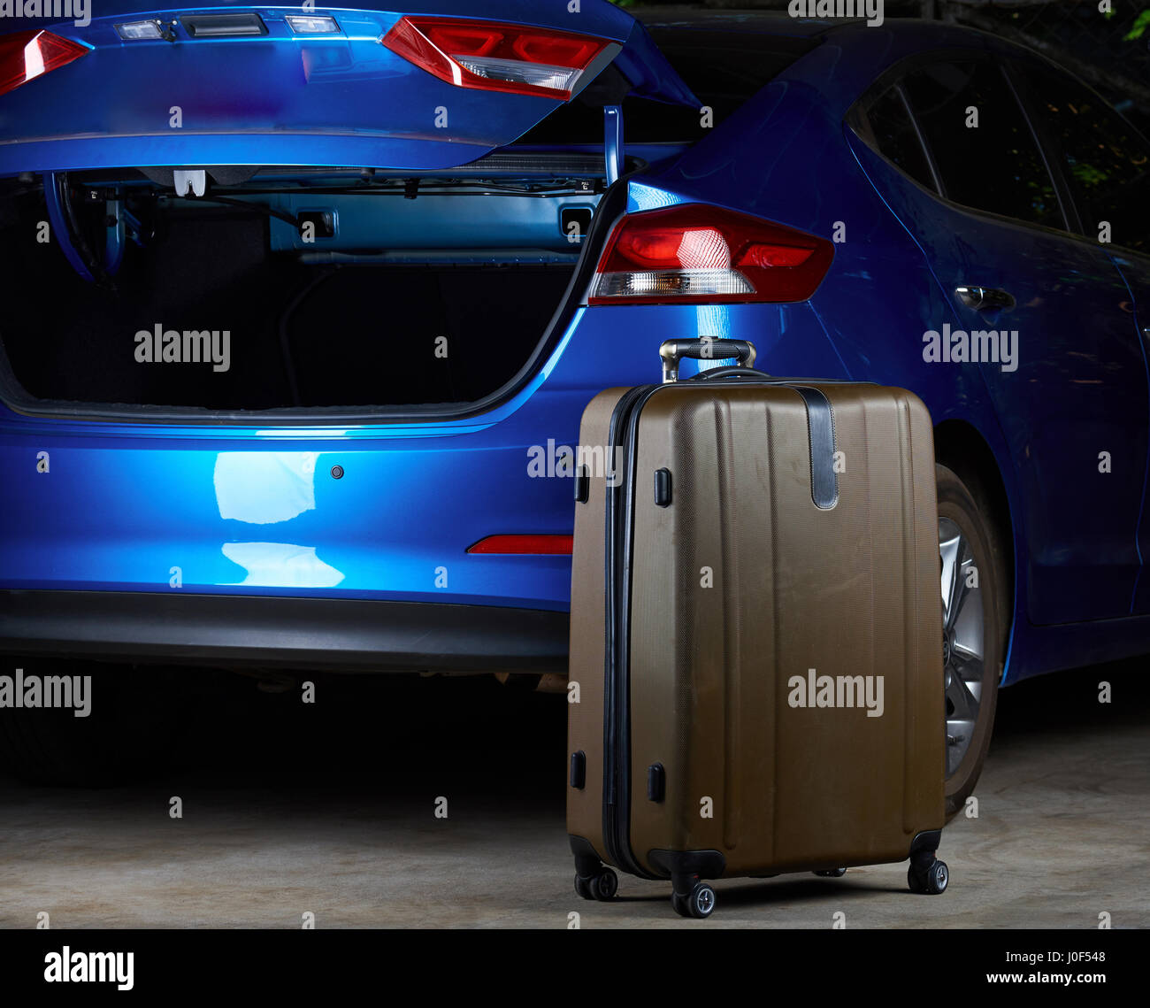 Brown luggage suitcase standing next to blue modern car with open trunk Stock Photo