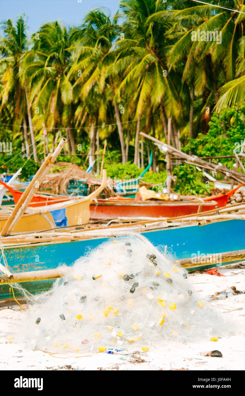 White fishing net on coral sand beach with colorful boats and palms in background Stock Photo