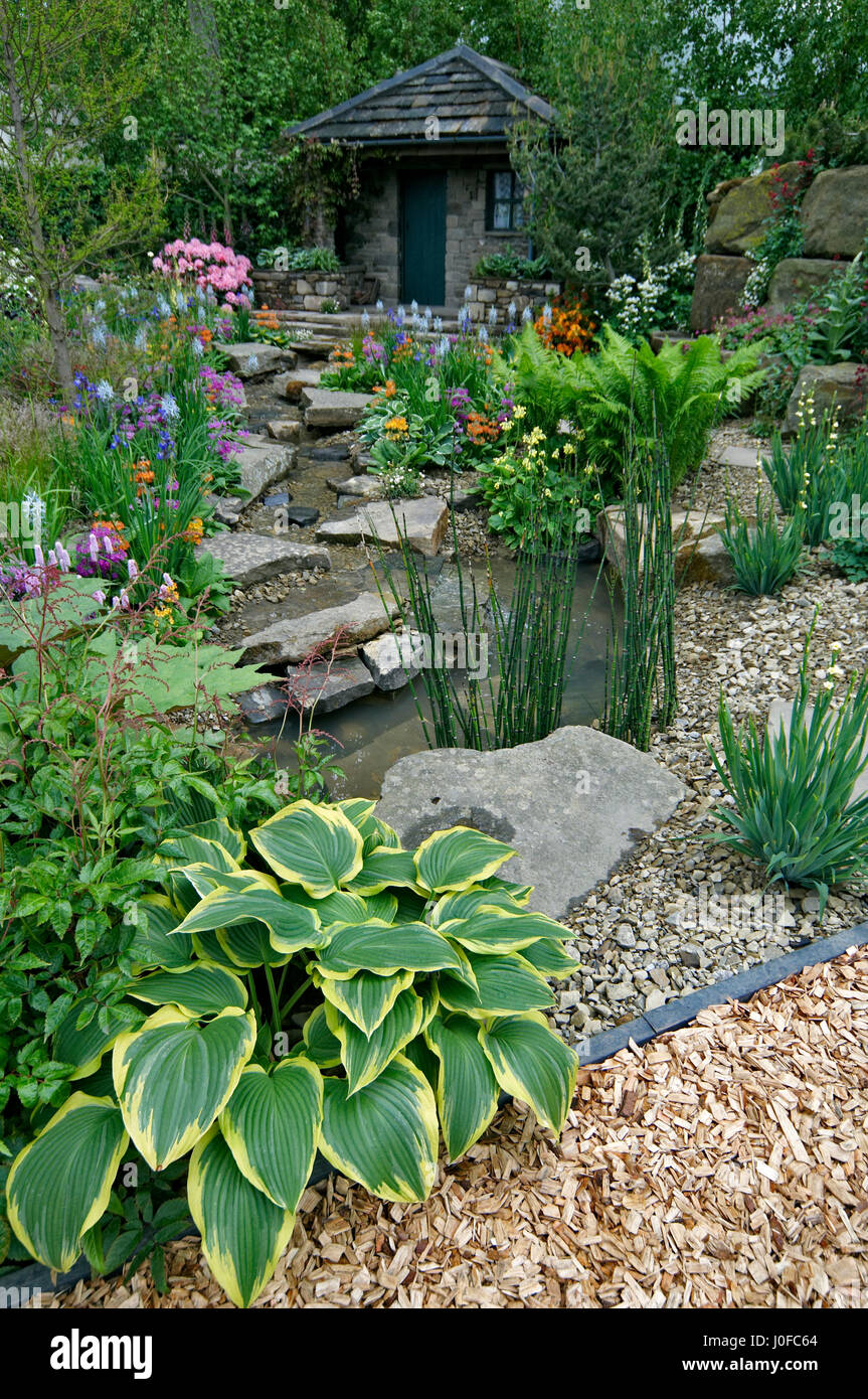 A country cottage garden in a wooded rockery with colourful planting Stock Photo