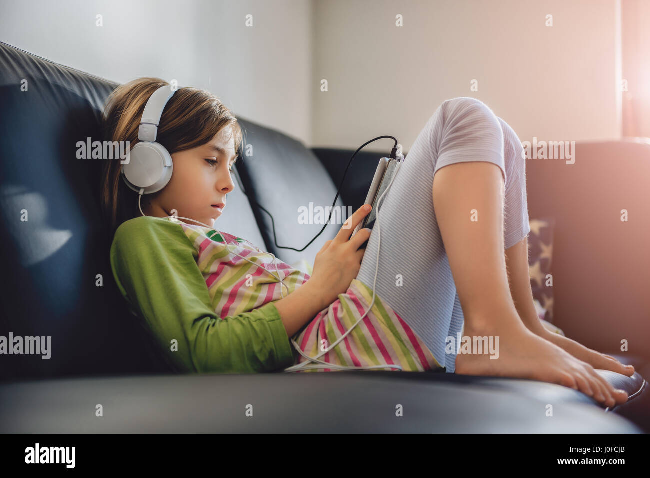 Girl sitting on black sofa using tablet and listening music Stock Photo