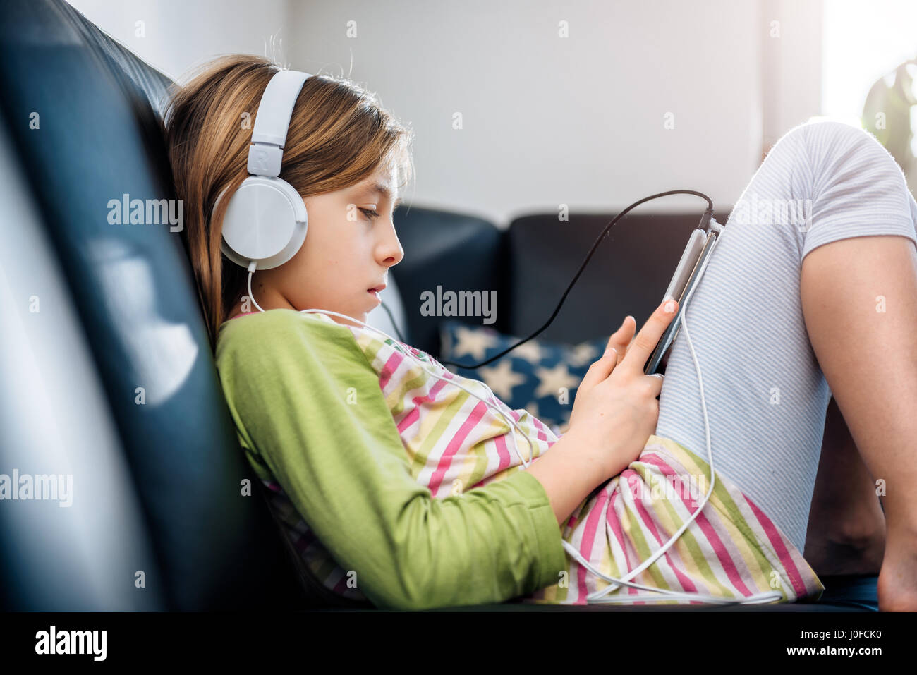 Girl sitting on black sofa using tablet and listening music Stock Photo