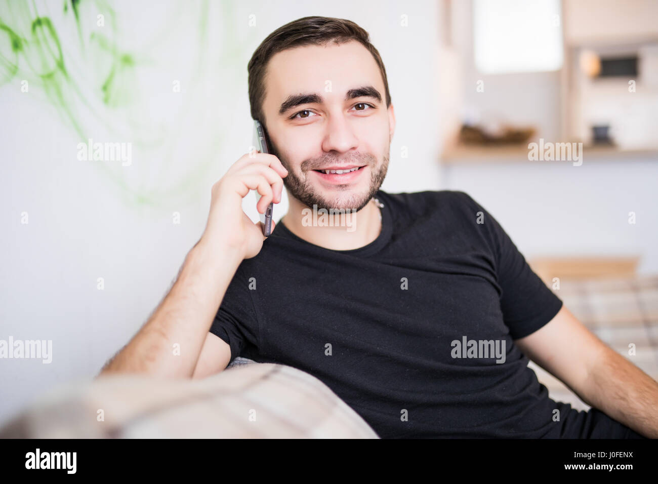 Young man on the cellphone sitting in the living room Stock Photo