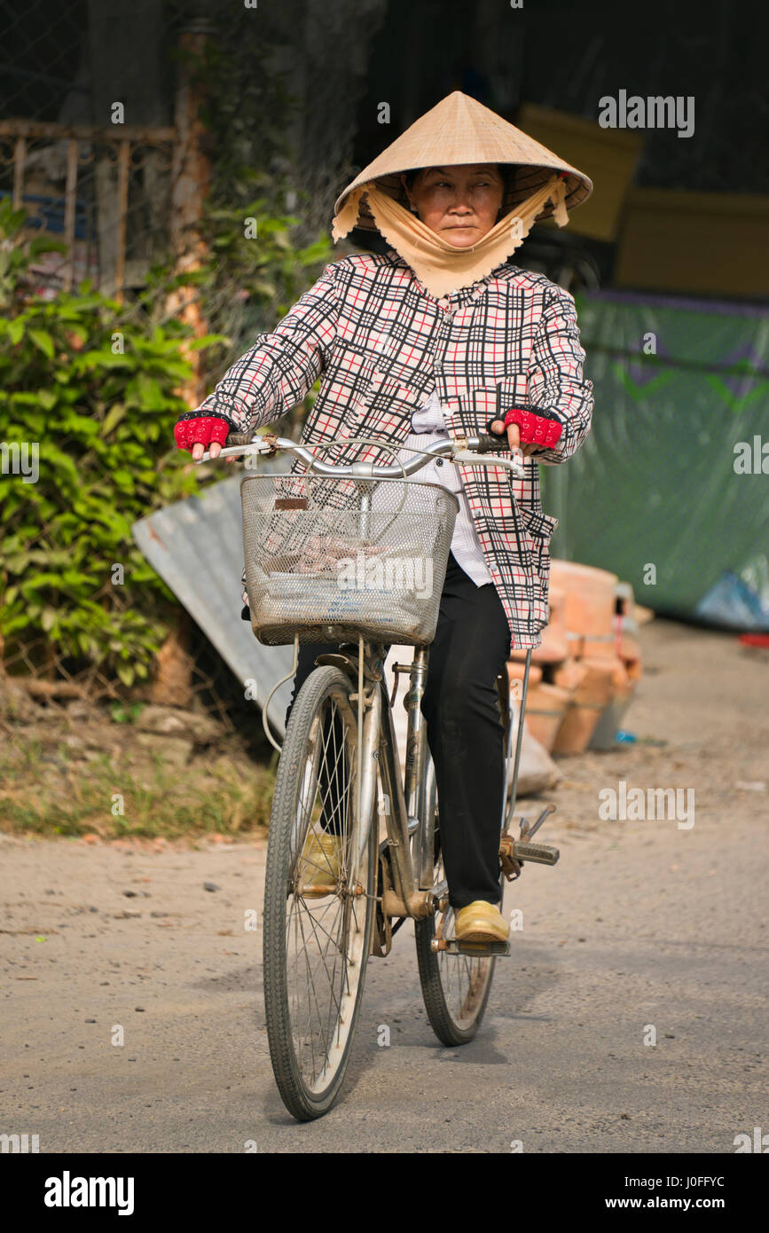 Vertical portrait of an old lady riding a bicycle through the streets in Hoi An, Vietnam. Stock Photo