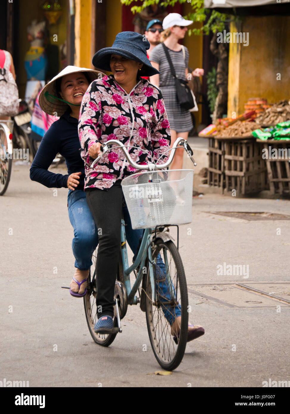 Vertical portrait of ladies riding bicycles through the streets in Hoi An, Vietnam. Stock Photo