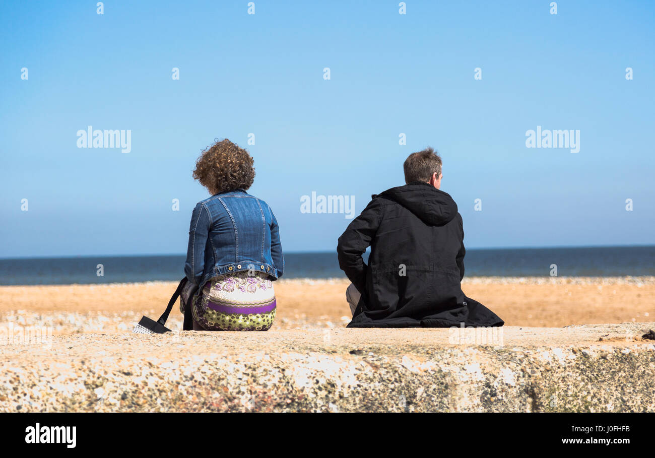 Sad depressed couple sitting back to each other on beach at sea. Horizontal ful frame crop with shallow depth of deep Stock Photo