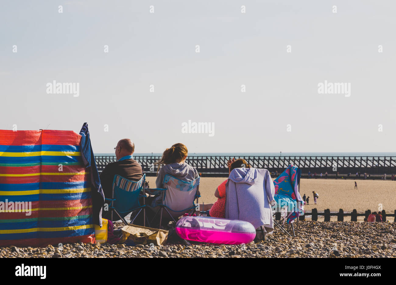 Family sitting and relaxing on stone beach in Littlehampton, England. Full frame horizotal crop with horizon in middle Stock Photo