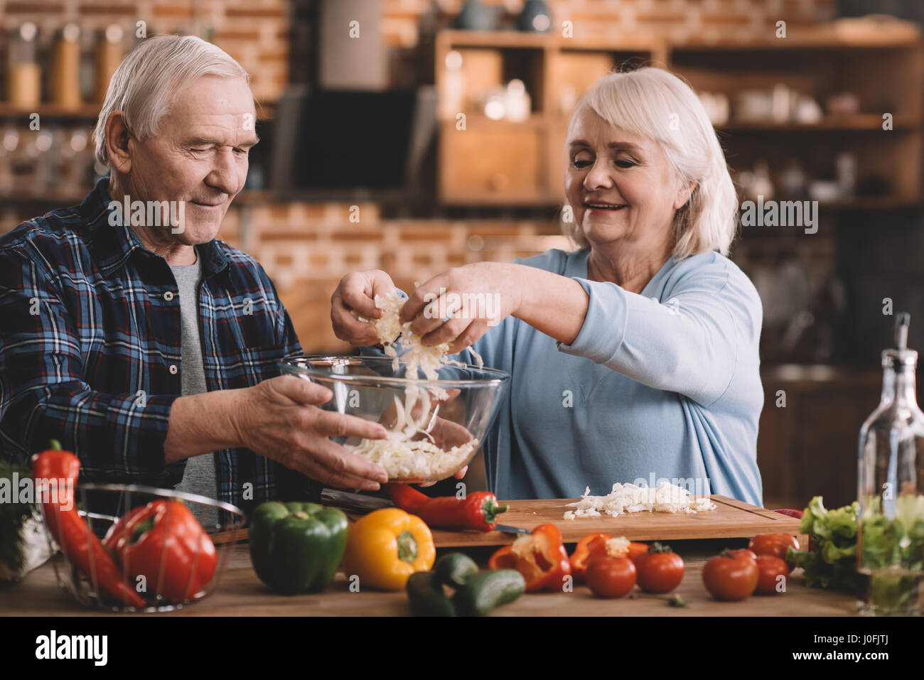 portrait of smiling senior couple making salad together in kitchen Stock Photo