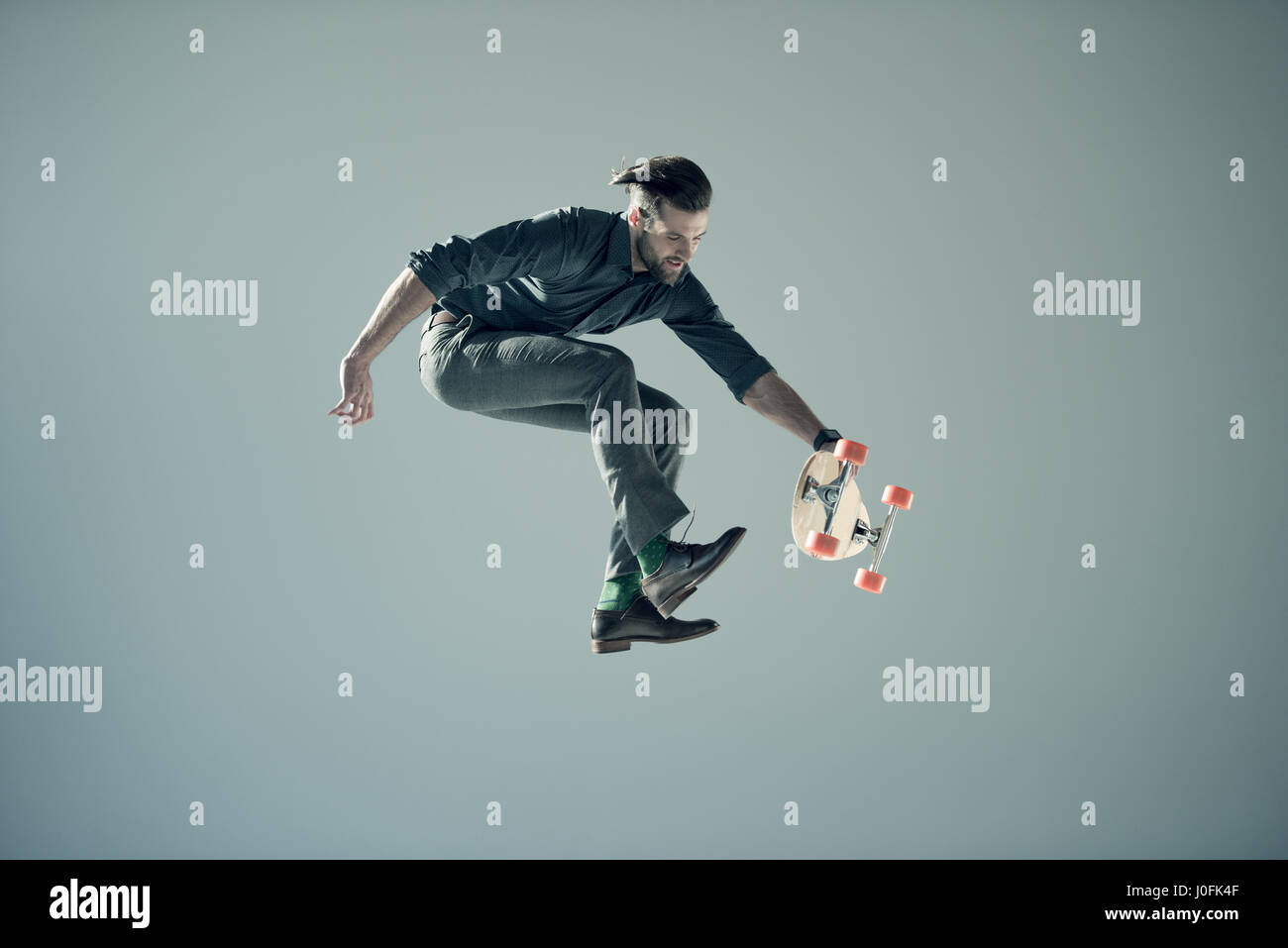 side view of jumping man holding skateboard on grey Stock Photo