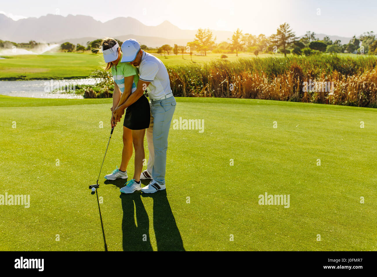 Male golf instructor teaching female golf player, personal trainer giving  lesson on golf course. Male showing woman to play golf Stock Photo - Alamy