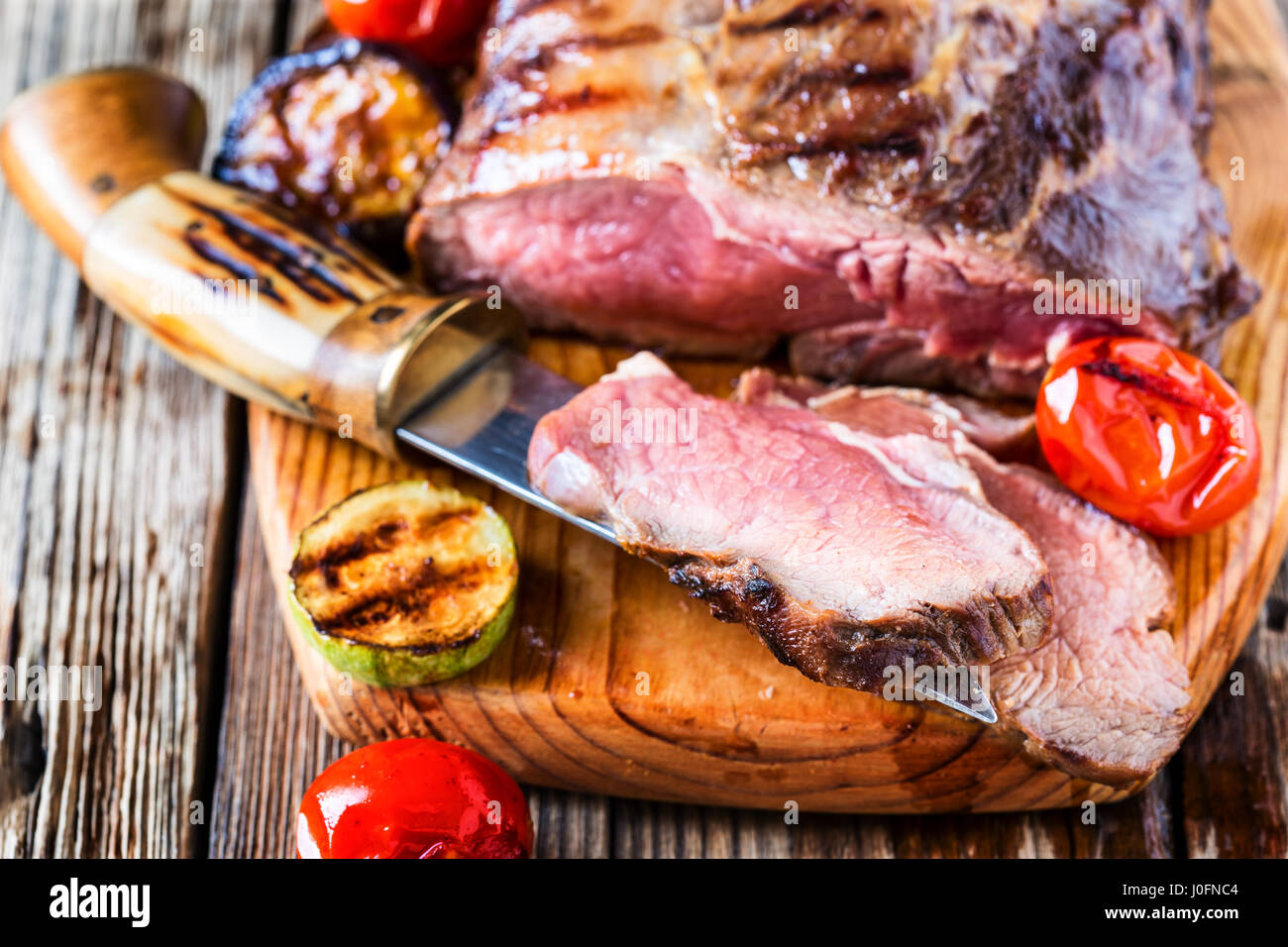 Rare roast sirloin of beef with roasted vegetables on rustic wooden background Stock Photo