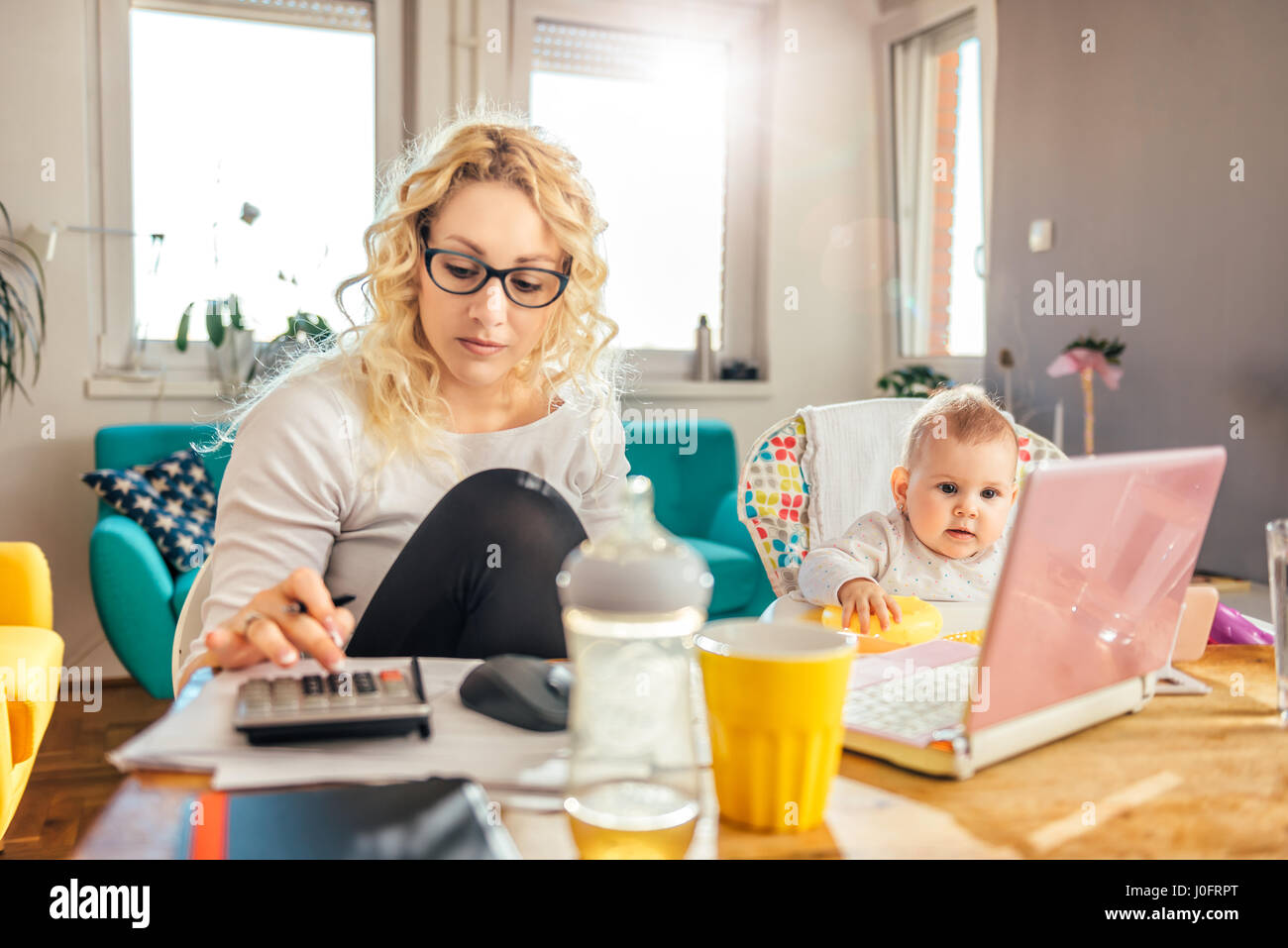 Little baby watching cartoon on smart phone while her mother doing paperwork at home Stock Photo