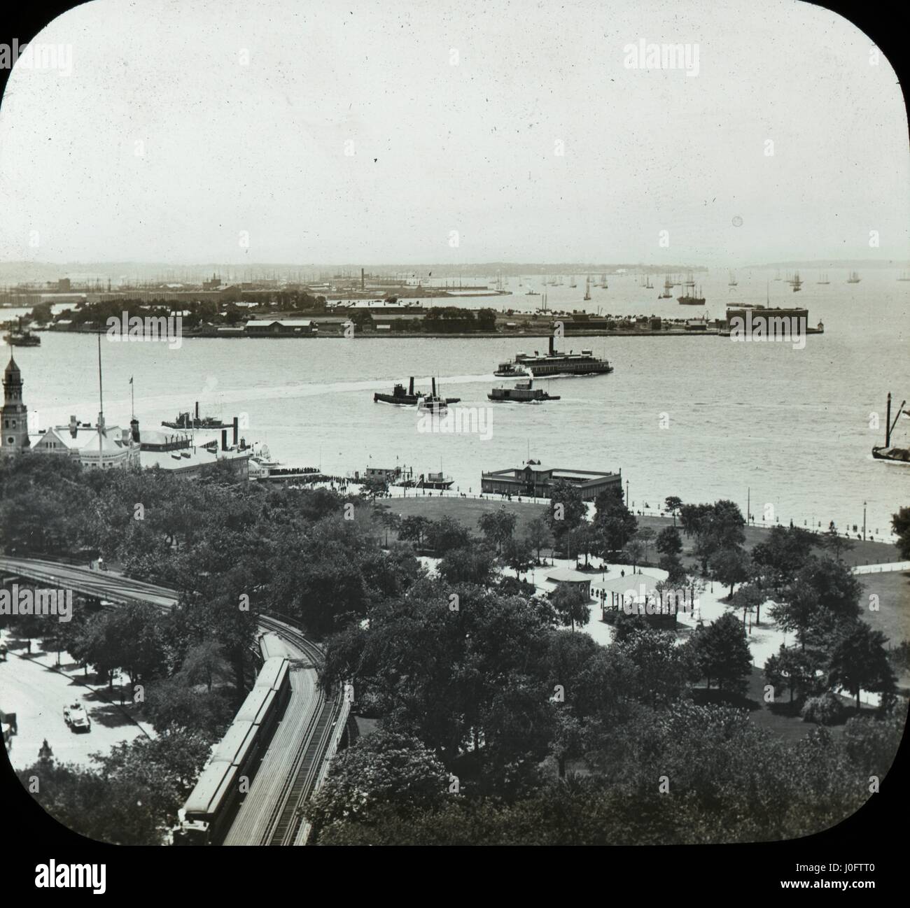 View onto a park, with train tracks in the foreground, bay with boats and islands in the distance Stock Photo