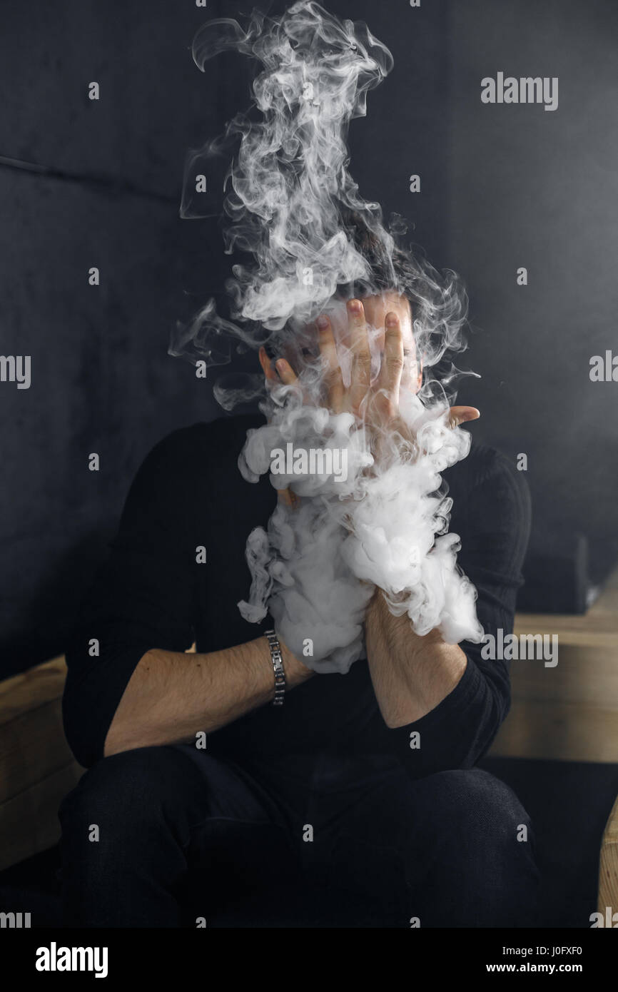 Vaping man holding a mod. A cloud of vapor. Black background. Stock Photo