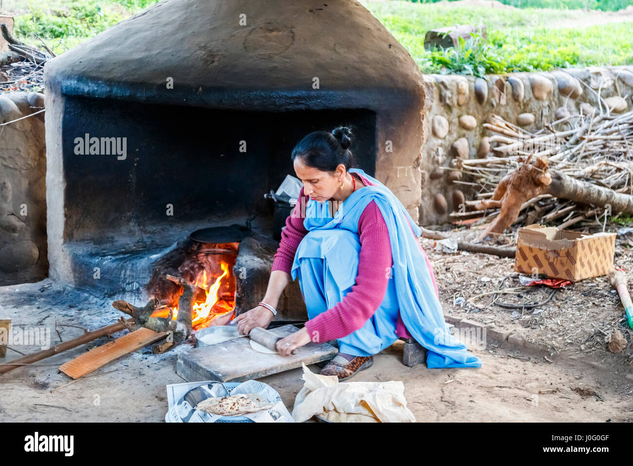 Local Indian woman wearing blue sari cooking chapatis in an oven with open fire, Judge's Court Hotel, Pragpur, Kagra district, Himachal Pradesh, India Stock Photo