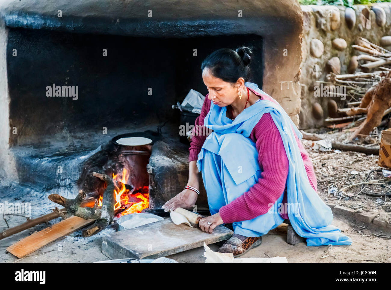 Local Indian woman wearing blue sari cooking chapatis in an oven with open fire, Judge's Court Hotel, Pragpur, Kagra district, Himachal Pradesh, India Stock Photo