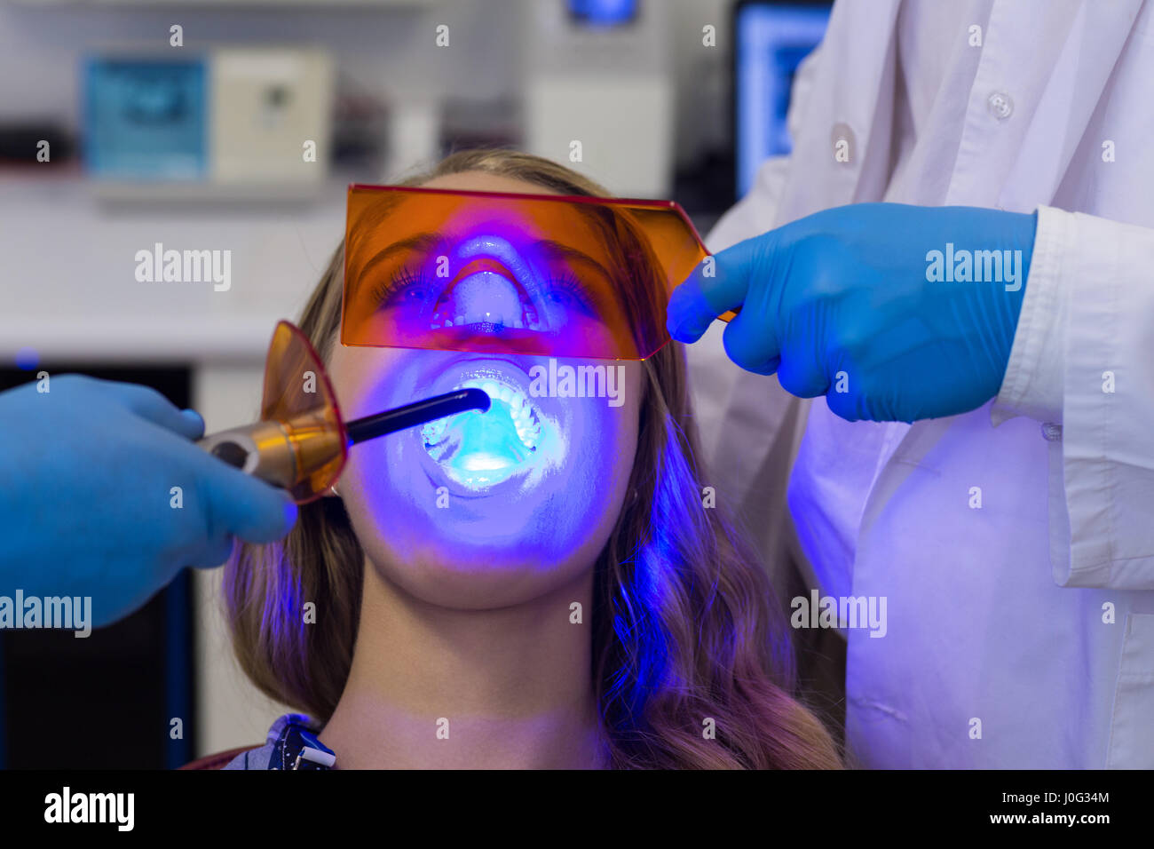 Dentists examining female patient with dental curing light in clinic