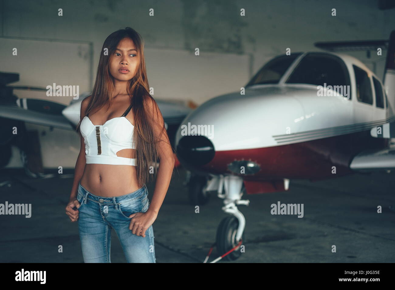 Beautiful female portrait in the airplane hangar, with modern aircraft Stock Photo