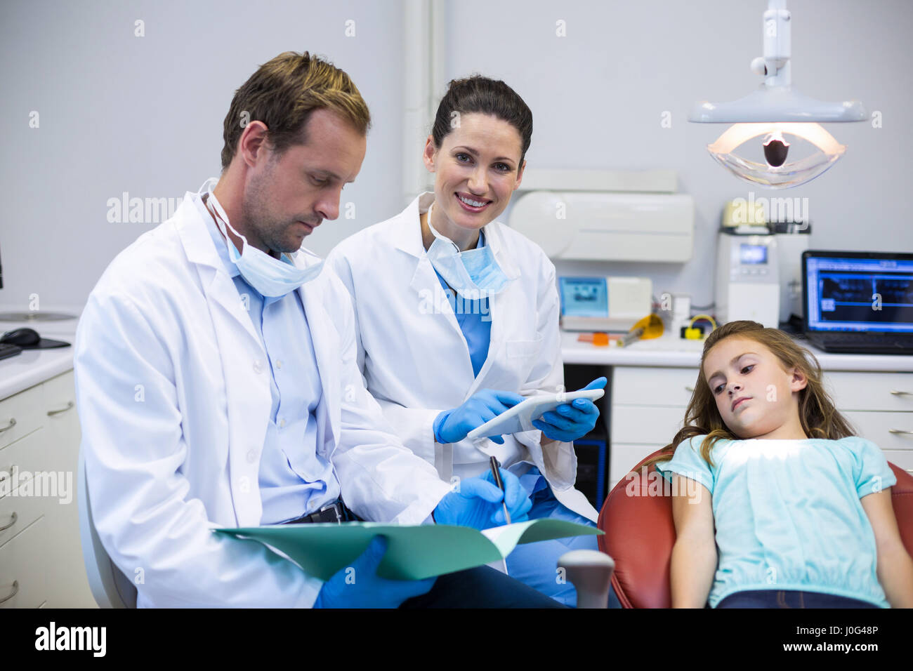 Dentists checking the reports while patient lying on dental chair in clinic Stock Photo