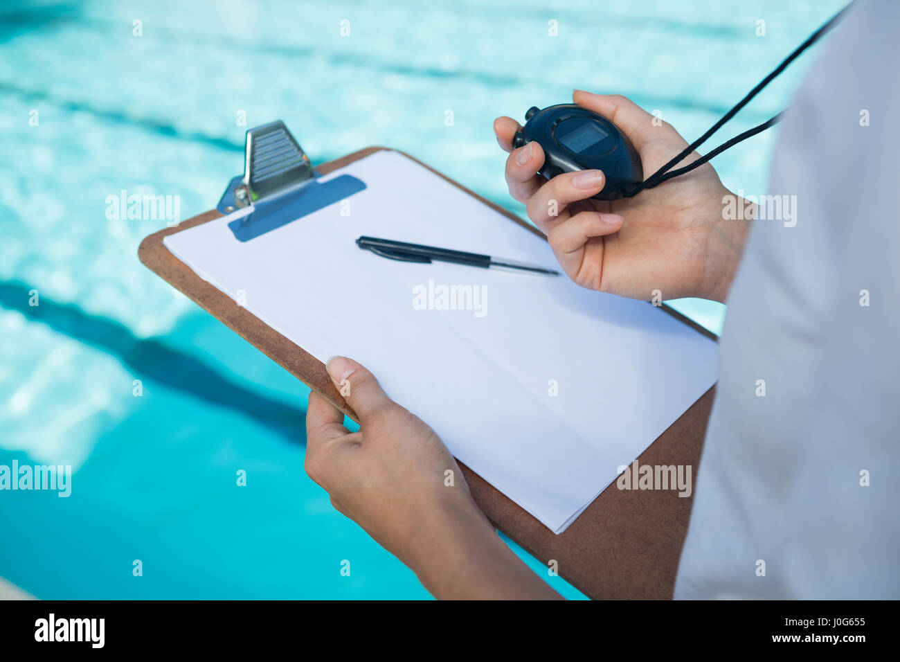 Mid section of swim coach looking at stopwatch at poolside Stock Photo