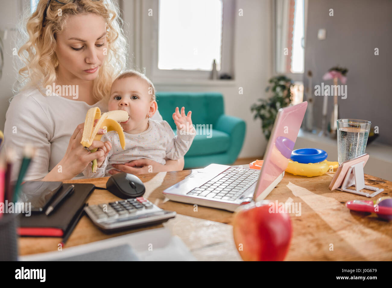 Mother feeding baby at home office with bananas Stock Photo