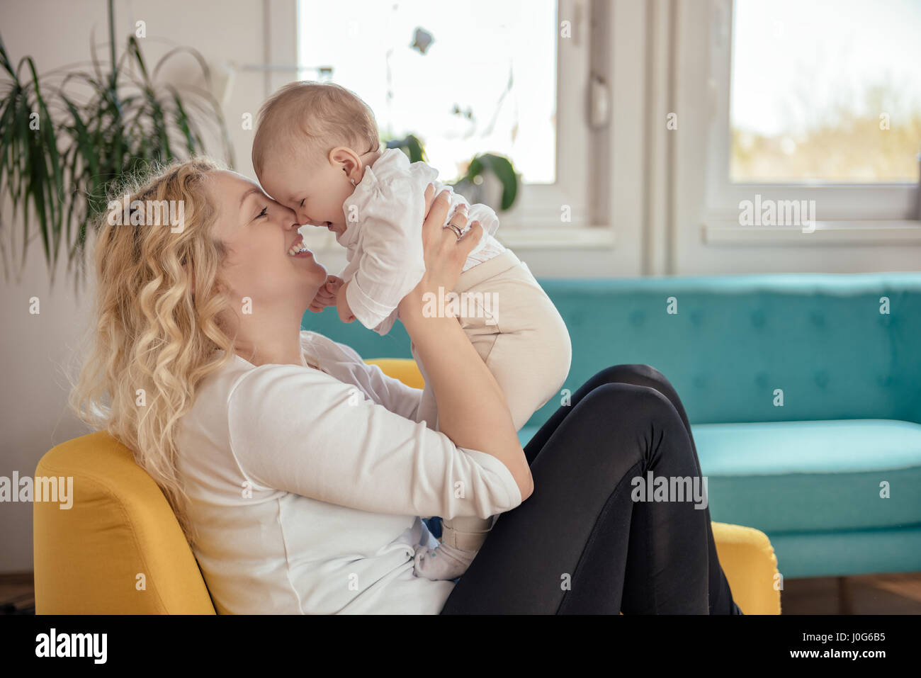 Mother and her baby head to head sitting at yellow armchair Stock Photo