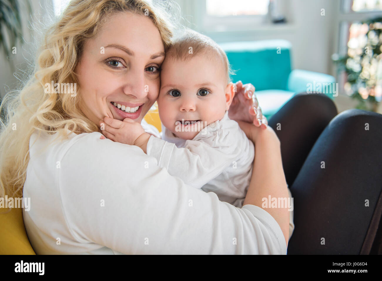 Mother holding baby in her arms and sitting at yellow armchair Stock Photo