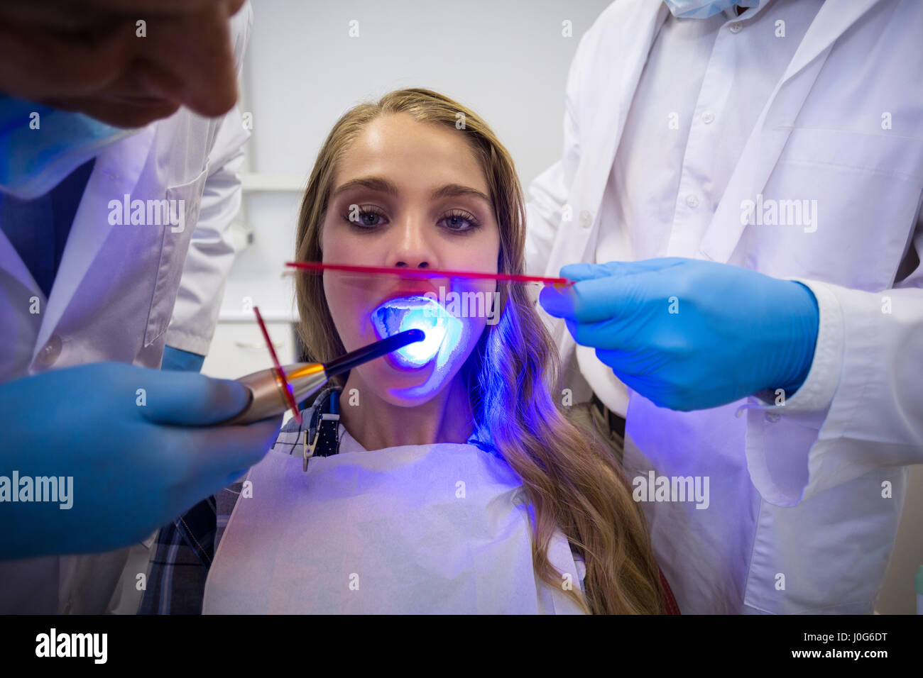 Dentists examining female patient with dental curing light in clinic