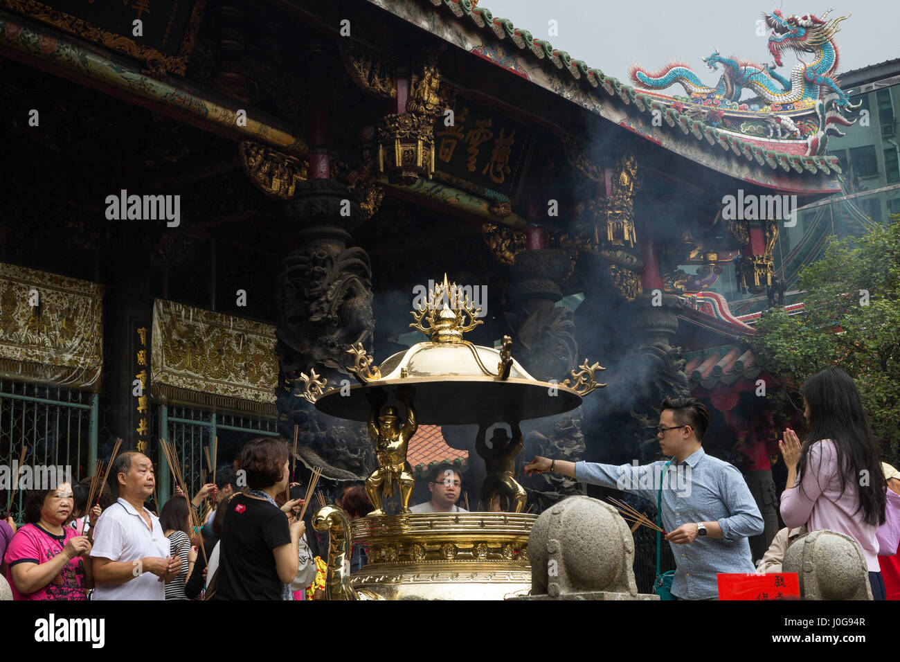 A lot of people praying with incense sticks by a golden incense burner at the Mengjia Longshan Temple in Taipei, Taiwan. Stock Photo