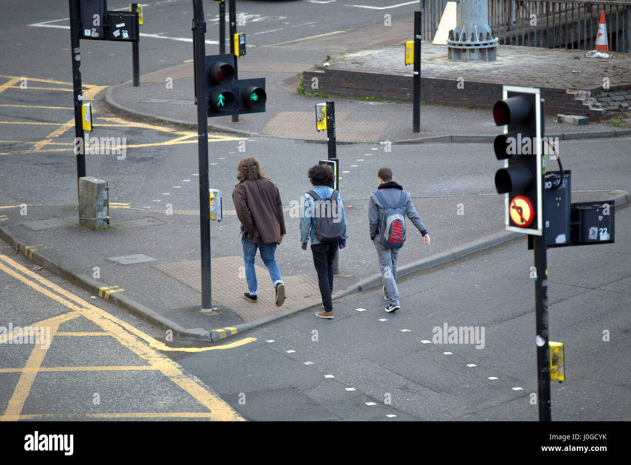 three 3 young teenage boys  students crossing road at green man on traffic lights Stock Photo