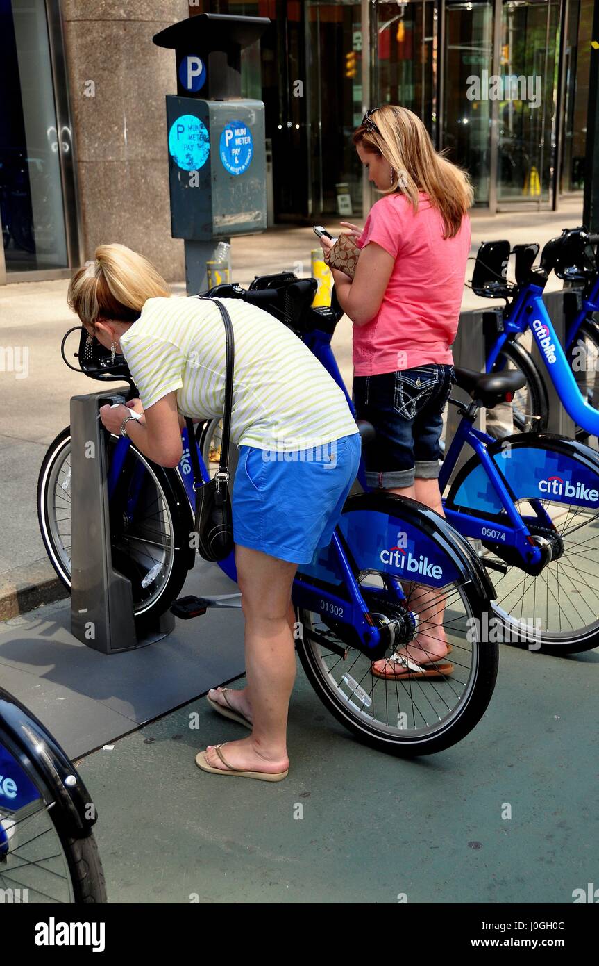 New York City - June 8, 2013:  Women checking out a Citibike from a docking station on Broadway at 55th Street while her friend checks her cell phone Stock Photo