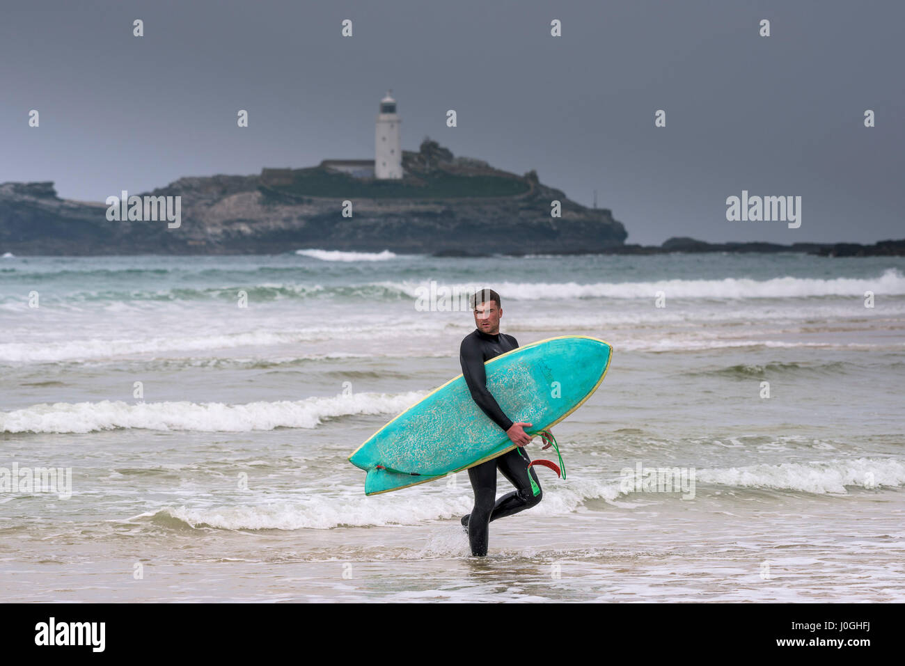 Gwithian Towans beach Sea Male Surfer Walking out of the sea Godrevy Lighthouse Carrying surfboard Coast Coastal Leisure activity Stock Photo