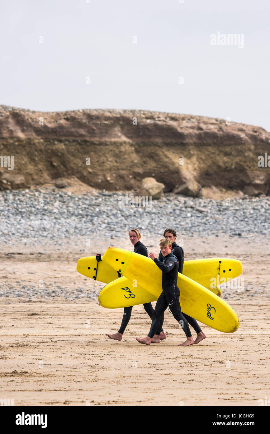 Cornwall. Three male surfers carrying their surfboards on Gwithian Towans beach. Stock Photo