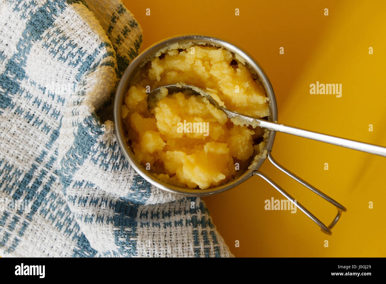 Ghee in stainless steel jar with a spoon on yellow background, top view