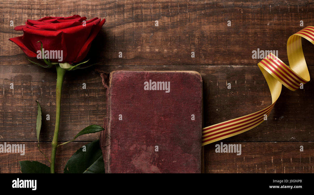 a red rose, an old book and a catalan flag, on a rustic wooden table, for Sant Jordi, the Catalan name for Saint Georges Day, when it is tradition to  Stock Photo