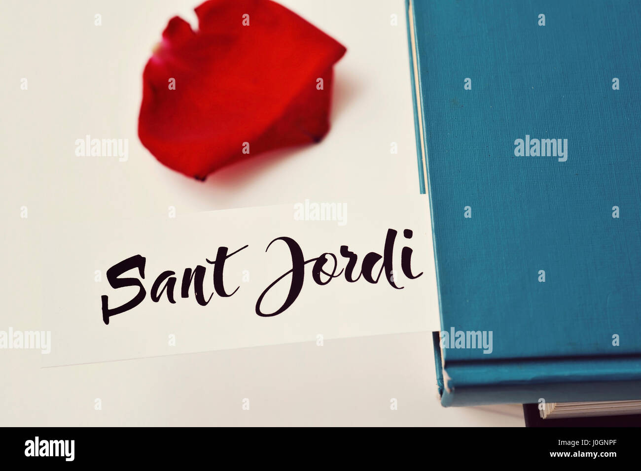 a red rose petal, a pile of books and the text Sant Jordi, the Catalan name for Saint Georges Day, when it is tradition to give red roses and books in Stock Photo