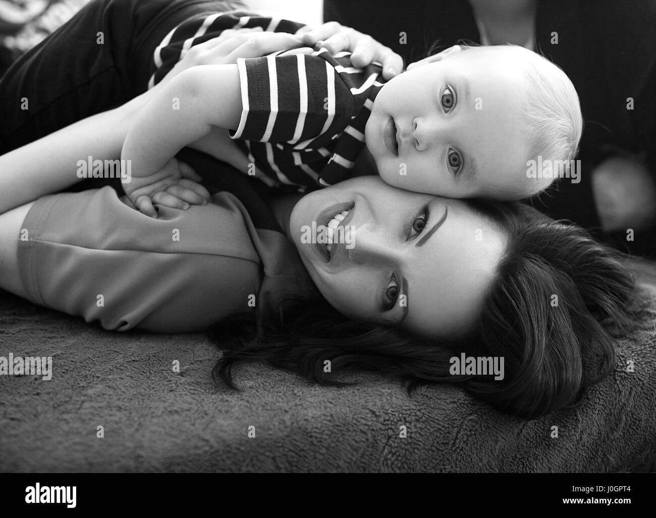 Young mother lies on bed with her baby and hugs him. Black and white image. Close up. Stock Photo