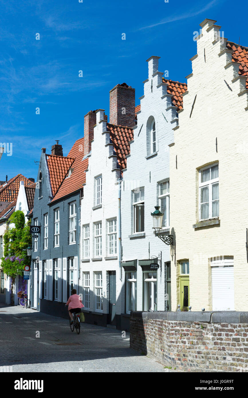 Cyclist riding past traditional painted houses with crow-stepped gables architecture in street scene in Bruges, Belgium Stock Photo