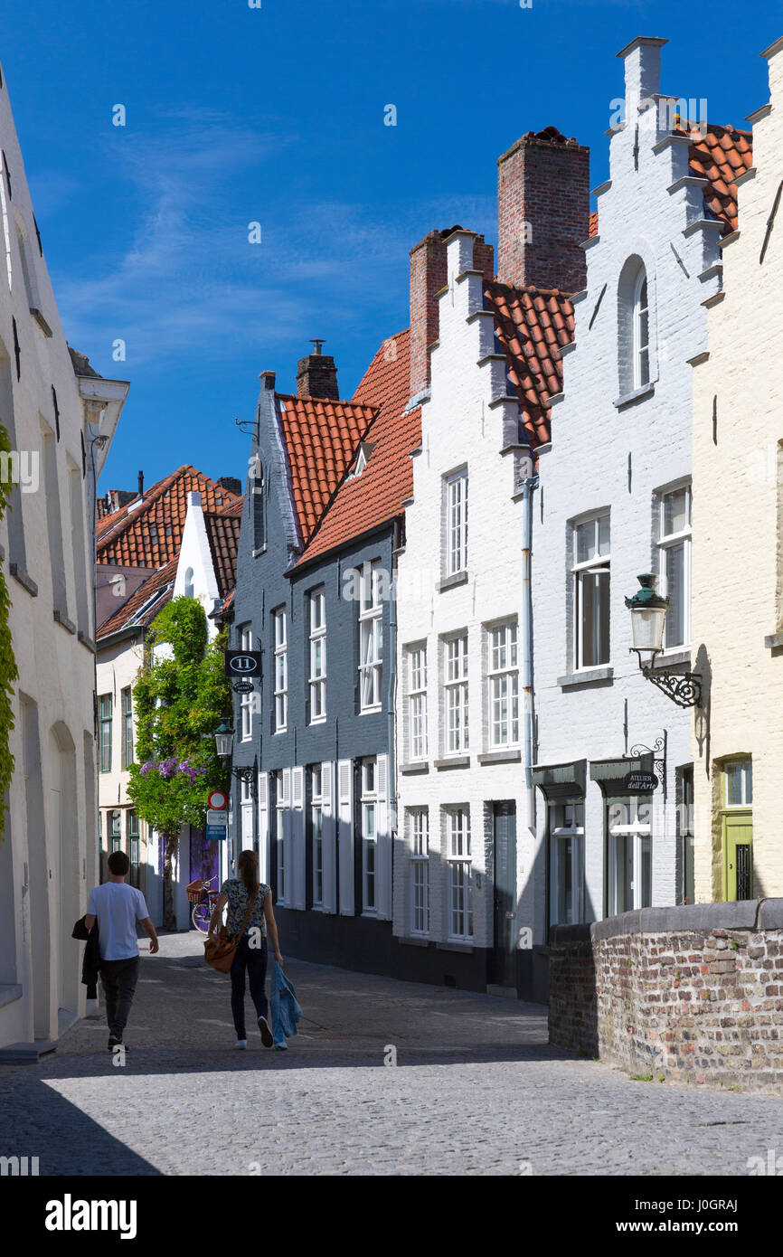 Couple walking past traditional architecture painted houses with crow-stepped gables - crow steps - in Bruges, Belgium Stock Photo